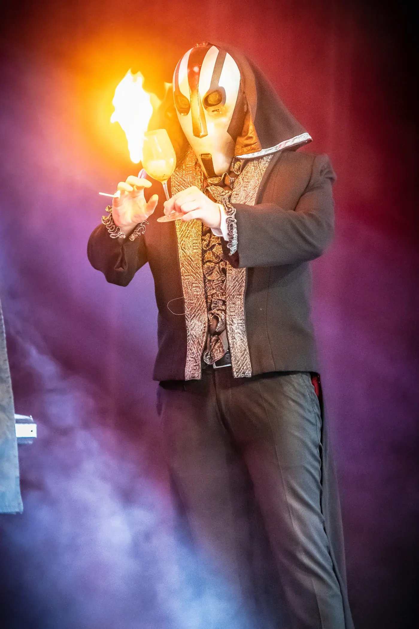 Magiker till sommarfest, mask och eld Illusionsshowens maskerade gestalt med eld i handen på scen